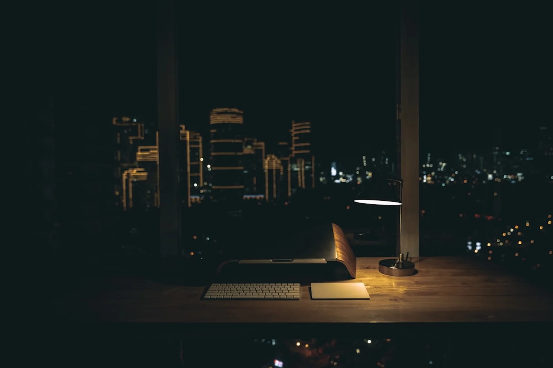 Dim office desk with laptop and headphones under soft lamp light during a night shift
