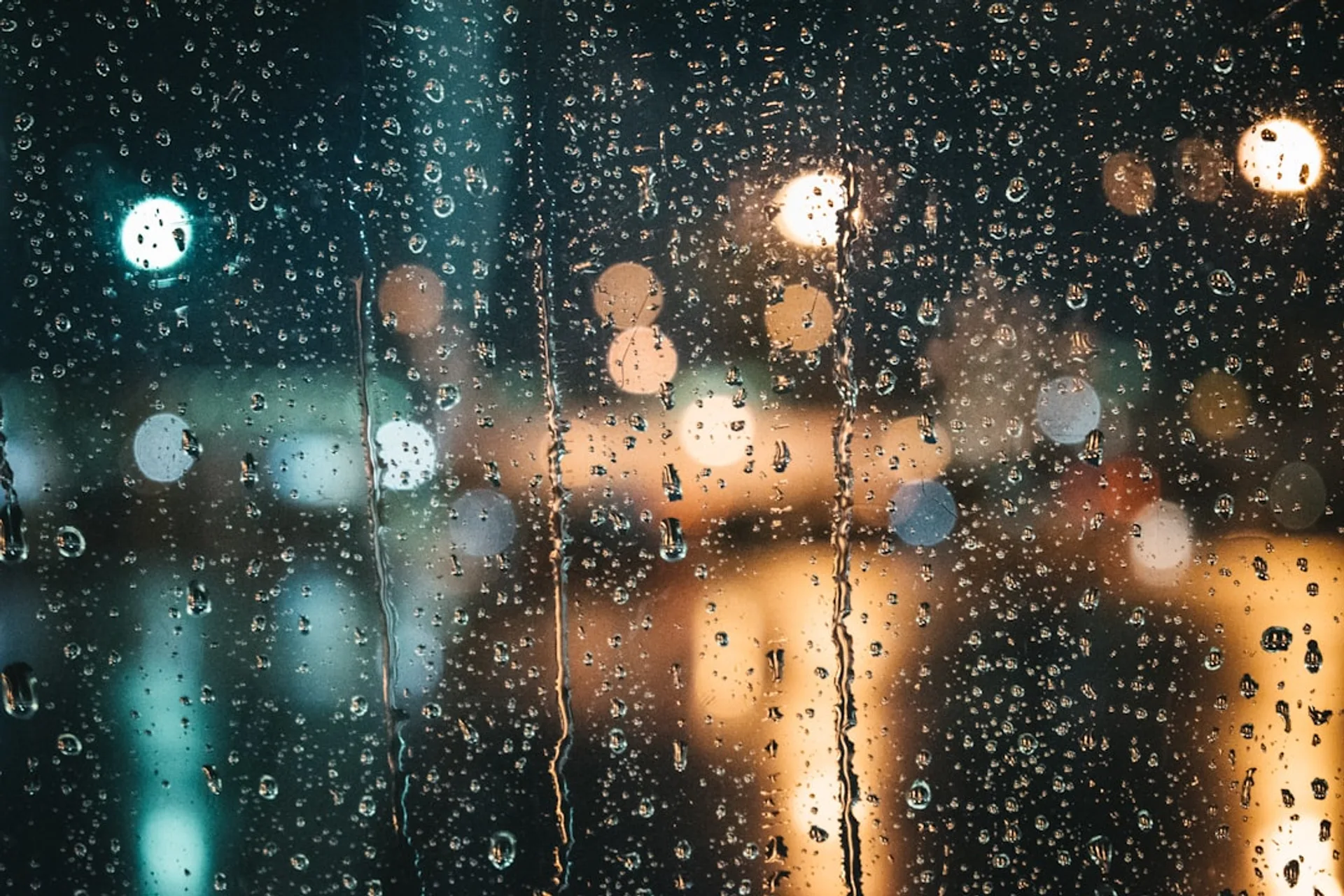 Raindrops on a window pane with blurred city lights in the background at night