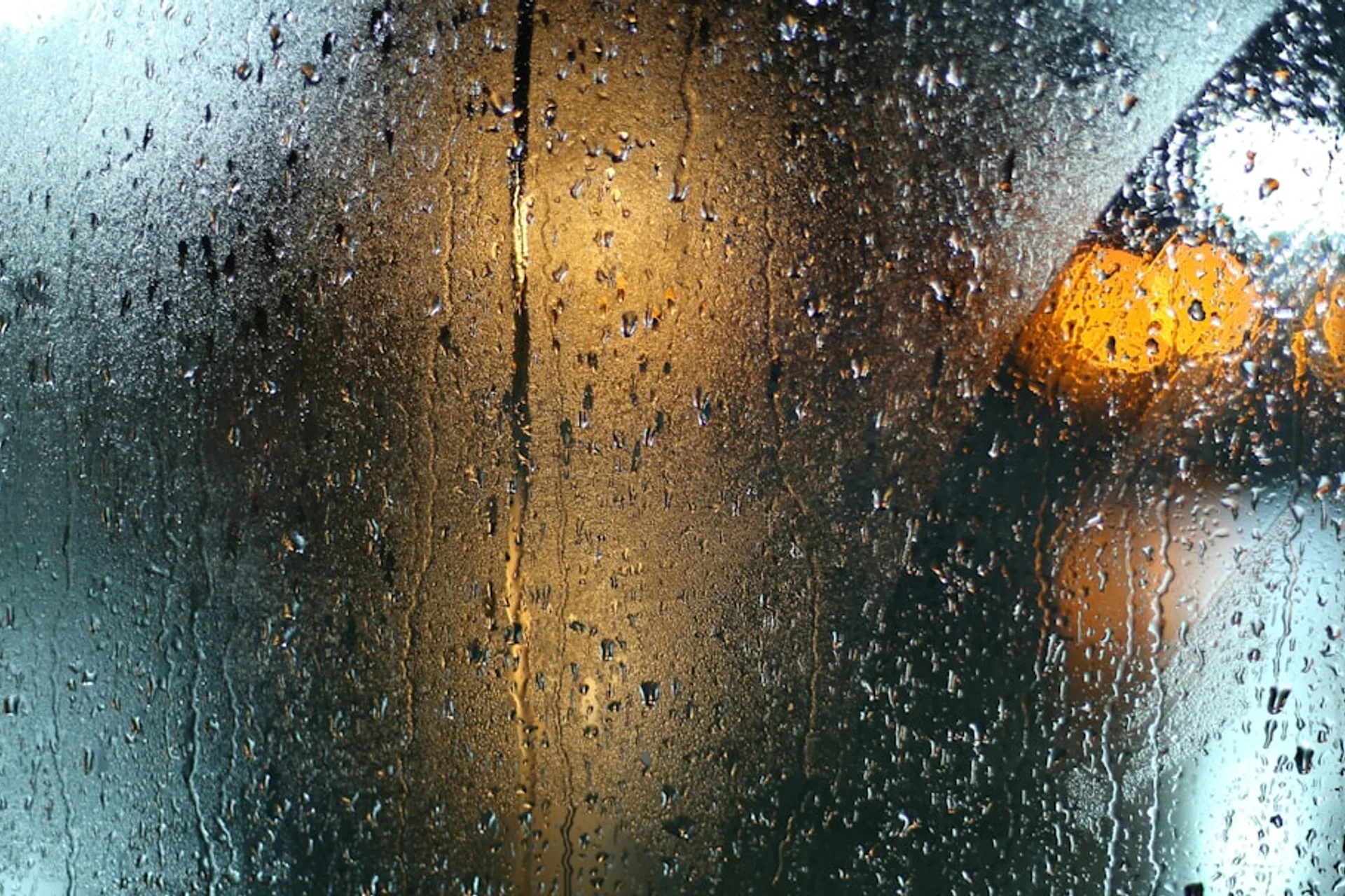 Dim workspace with headphones, soft lamp glow, and rain streaks on window