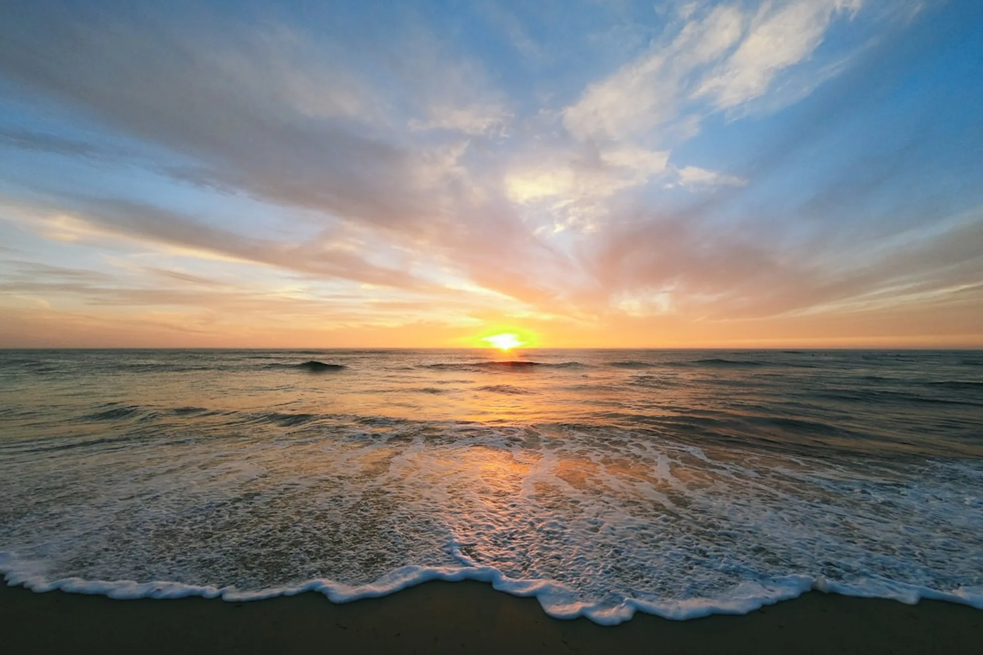 Gentle ocean waves rolling onto a sandy shore under a pastel sunset sky